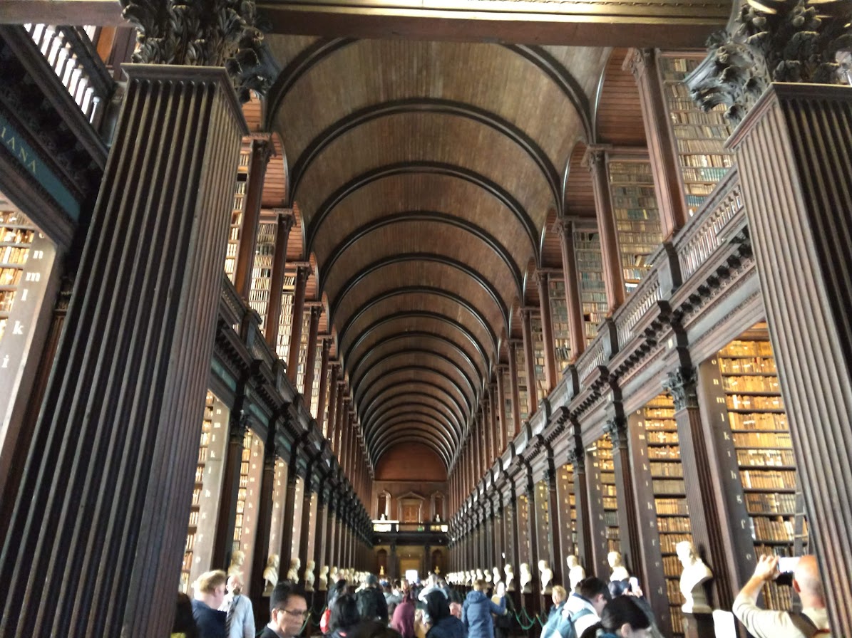 image of Trinity College Dublin's Long Room. This is a large, two story room with a barrel vault ceiling. The two stories are covered with thousands of archival and rare books. Each row of books has a bust on the end.