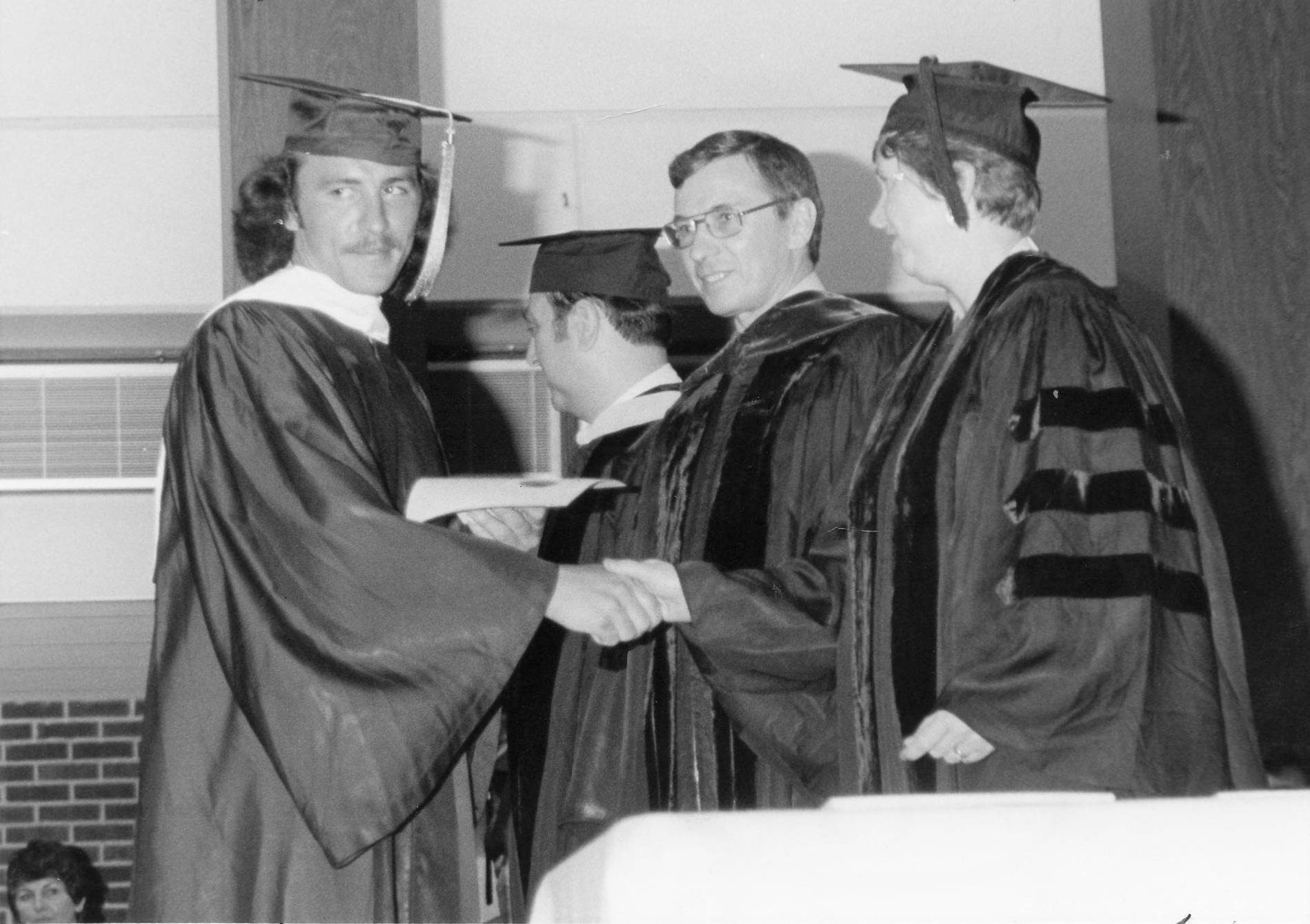 This a black and white image of a student receiving a handshake at graduation by the president.