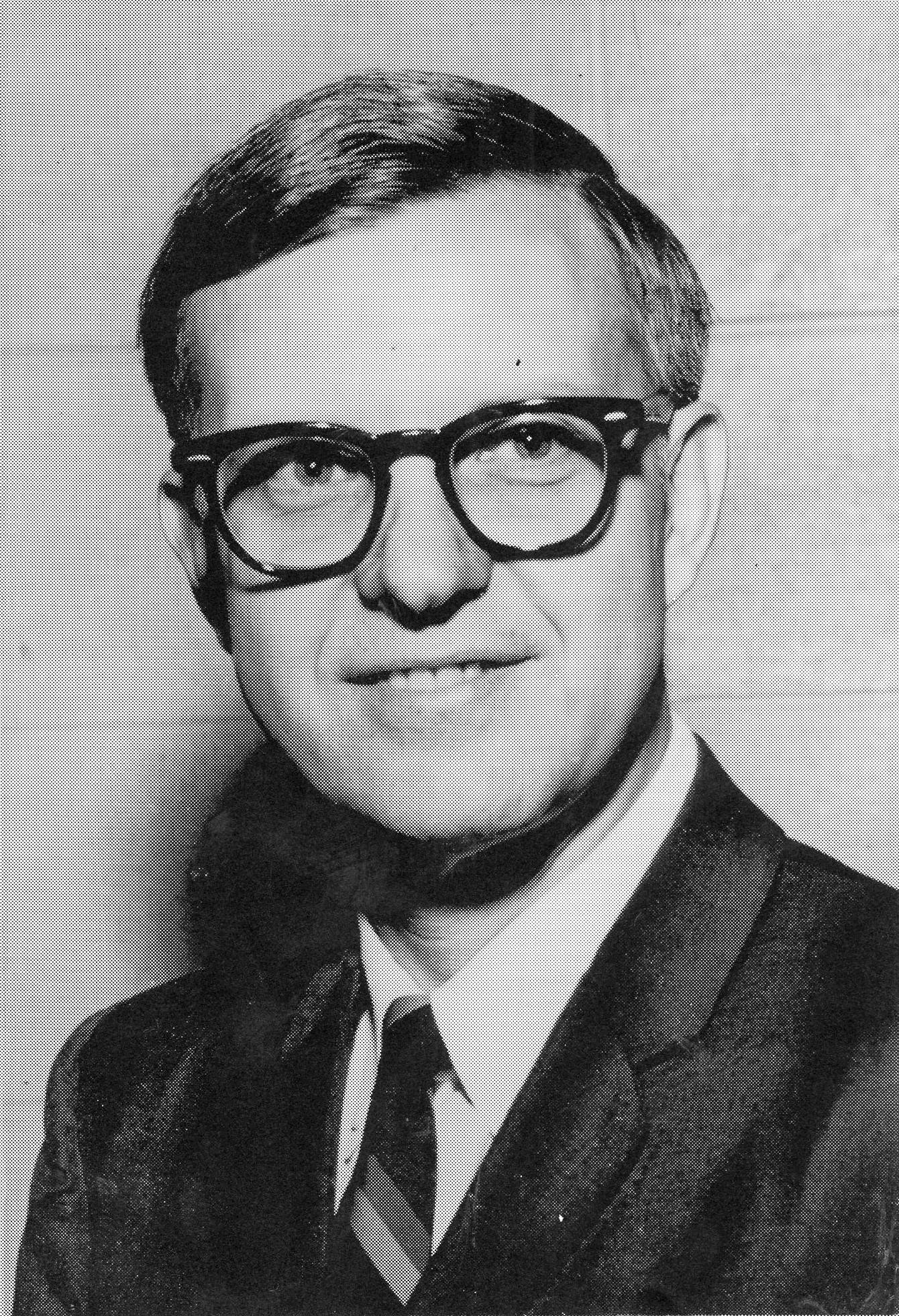 This a black and white image of a white man with glasses in a suit.