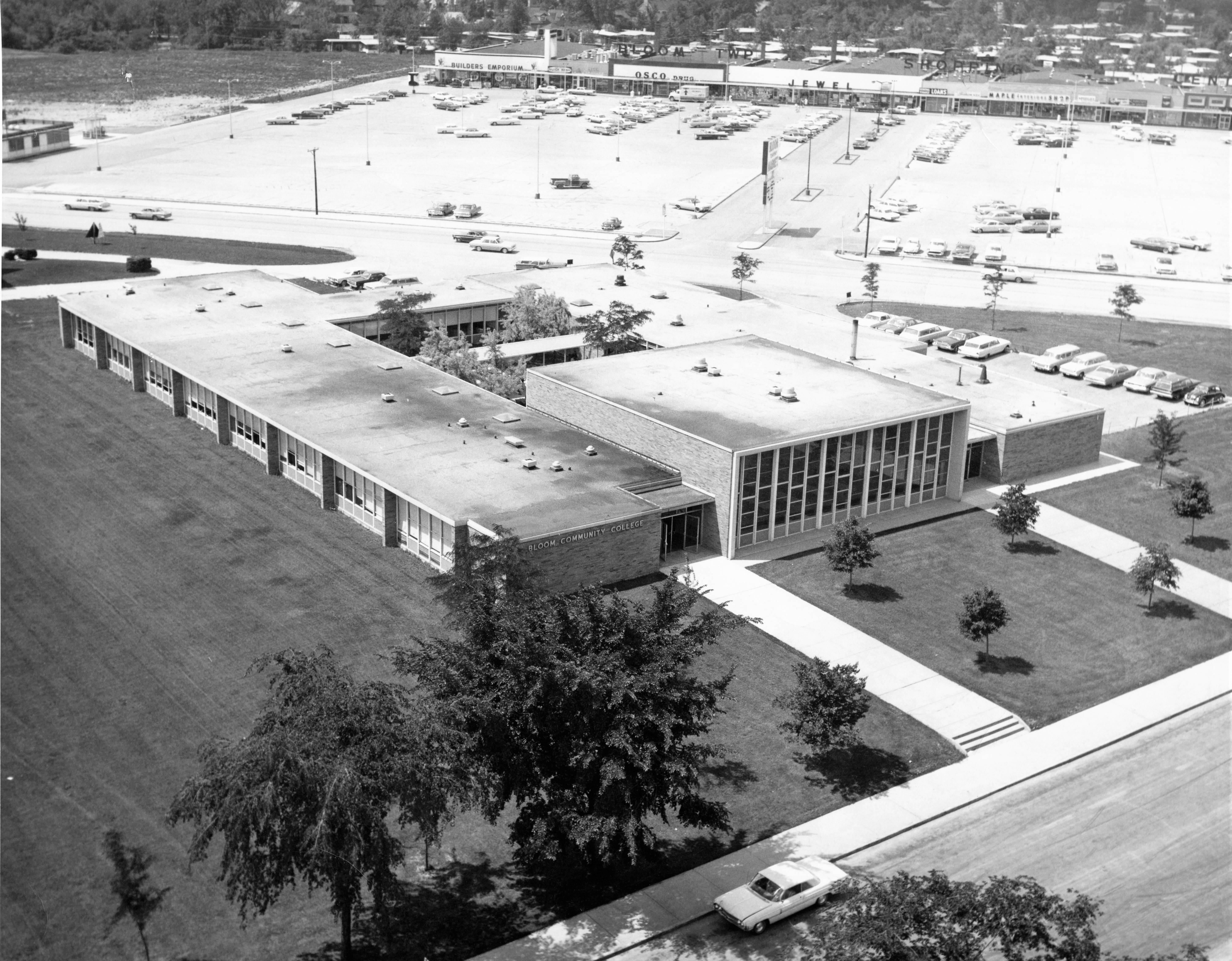 This image is an aerial view of Bloom Township Junior College. It is a black and white picture of a mid-century, glass structure.